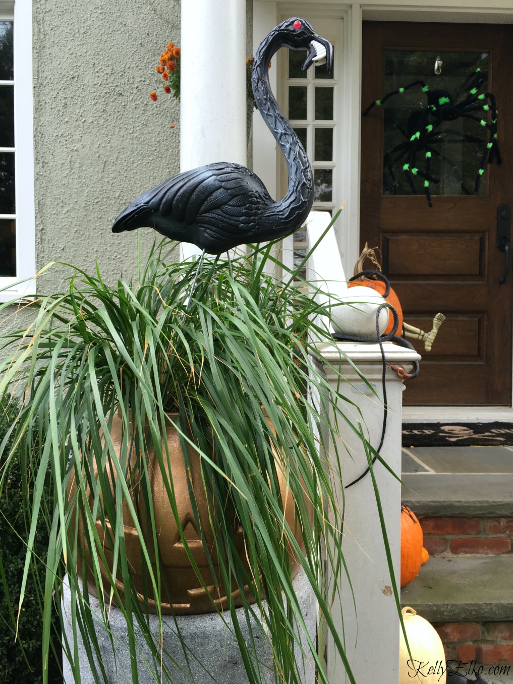 Love this Halloween porch with plastic pumpkin planter and zombie flamingos kellyelko.com #flamingo #halloween #halloweendecor #halloweenplanter #fallplanter #fall #pumpkindecor #pumpkinplanter #flamingo 