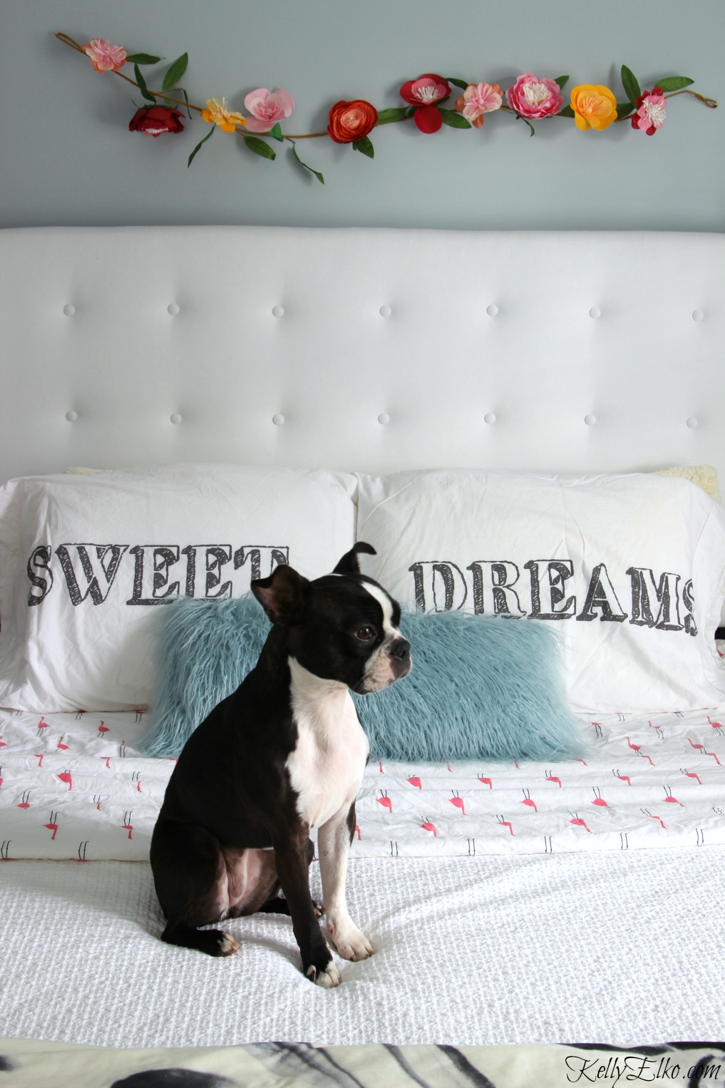 White tufted headboard gives this blue bedroom a glam look and I love the paper flower garland kellyelko.com