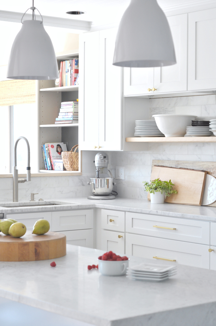 White marble kitchen with wood floating shelves and brass cabinet pulls