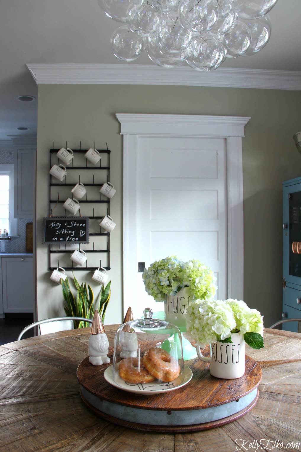 Love this farmhouse kitchen with modern bubble glass chandelier, farmhouse table and huge wall mounted bottle drying rack kellyelko.com