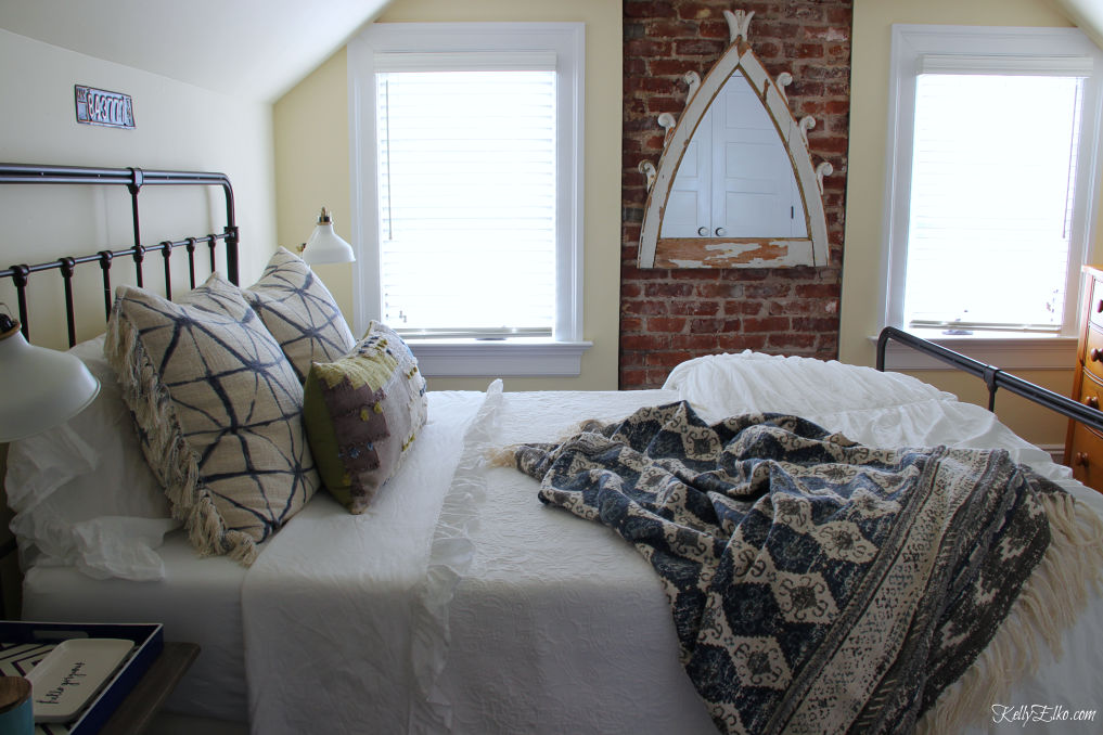 Guest Bedroom Decor - love the exposed brick wall and black iron bed and white bedding with lots of fun pillows kellyelko.com #bedroom #bedroomdecor #bedroomfurniture #bedroomdecorating #guestbedroom 