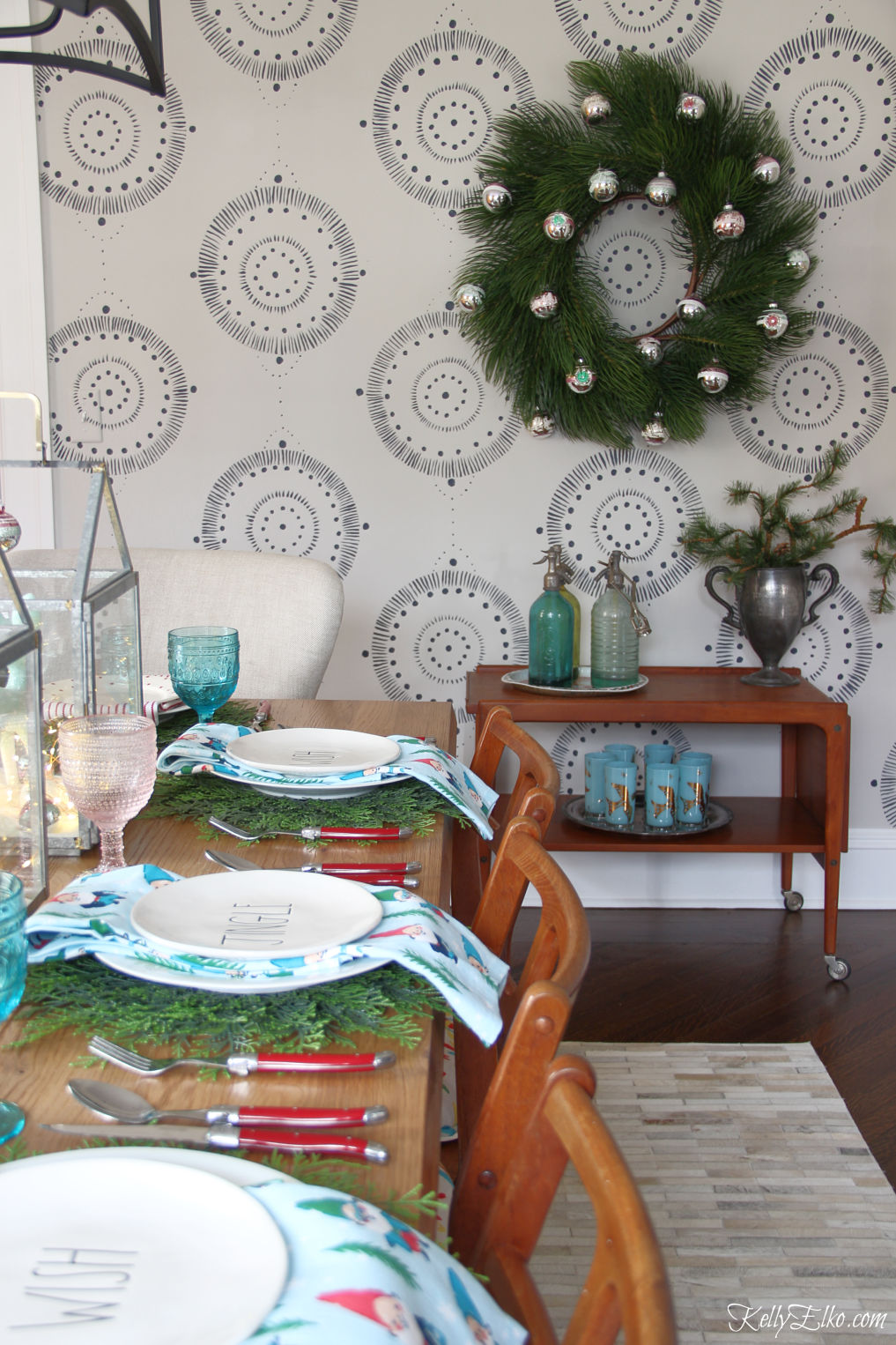 Love this dining room at Christmas with non traditional colors and vintage bar cart with huge wreath of Shiny Brites kellyelko.com #christmasdecor #christmaswreath #christmasdecorations #vintagechristmas #shinybrites #retrochristmas #wallmural #ltkholiday