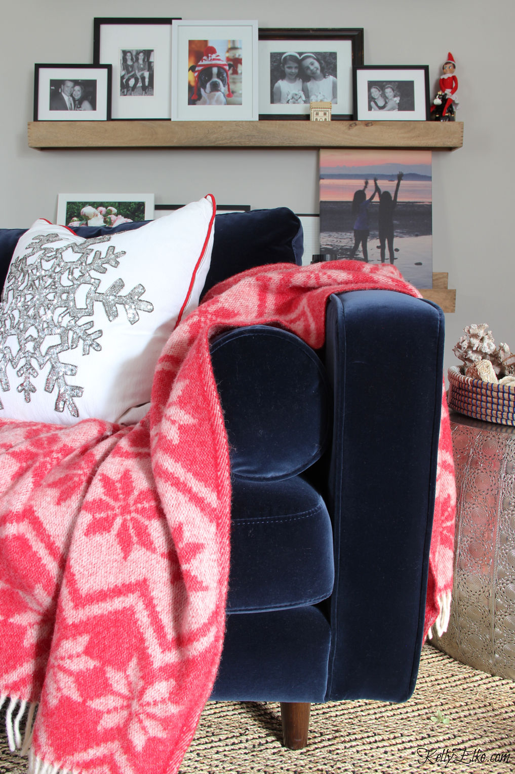 Love this cozy blue velvet sofa with red throw and the gallery wall of family photos kellyelko.com #christmas #christmasdecor #bohochristmas #christmaspillows #gallerywall 