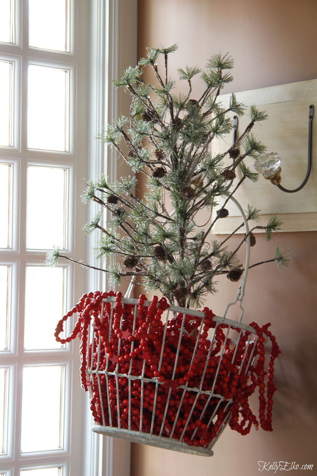 Love this Christmas tree in a wire basket filled with red garland kellyelko.com #christmastree #christmasdecor #christmasgarland #christmasdecorations #farmhousechristmas 