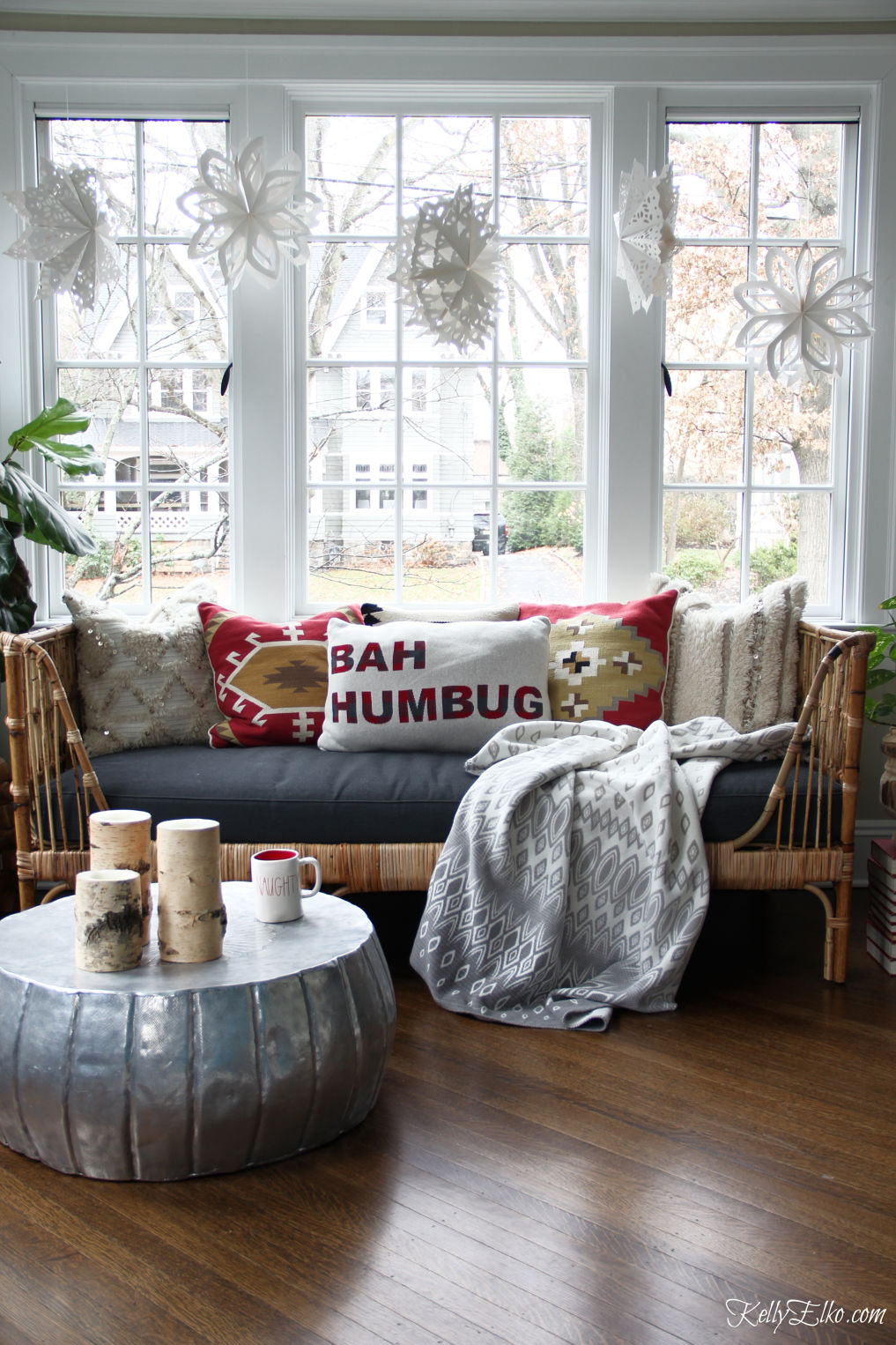 Love this Christmas sunroom with paper snowflakes hanging above a boho rattan daybed kellyelko.com #christmas #christmasdecor #christmasdecorating #christmaspillows #boho #bohodecor #eclecticdecor #interiordecor #interiordecorate #sunroom 