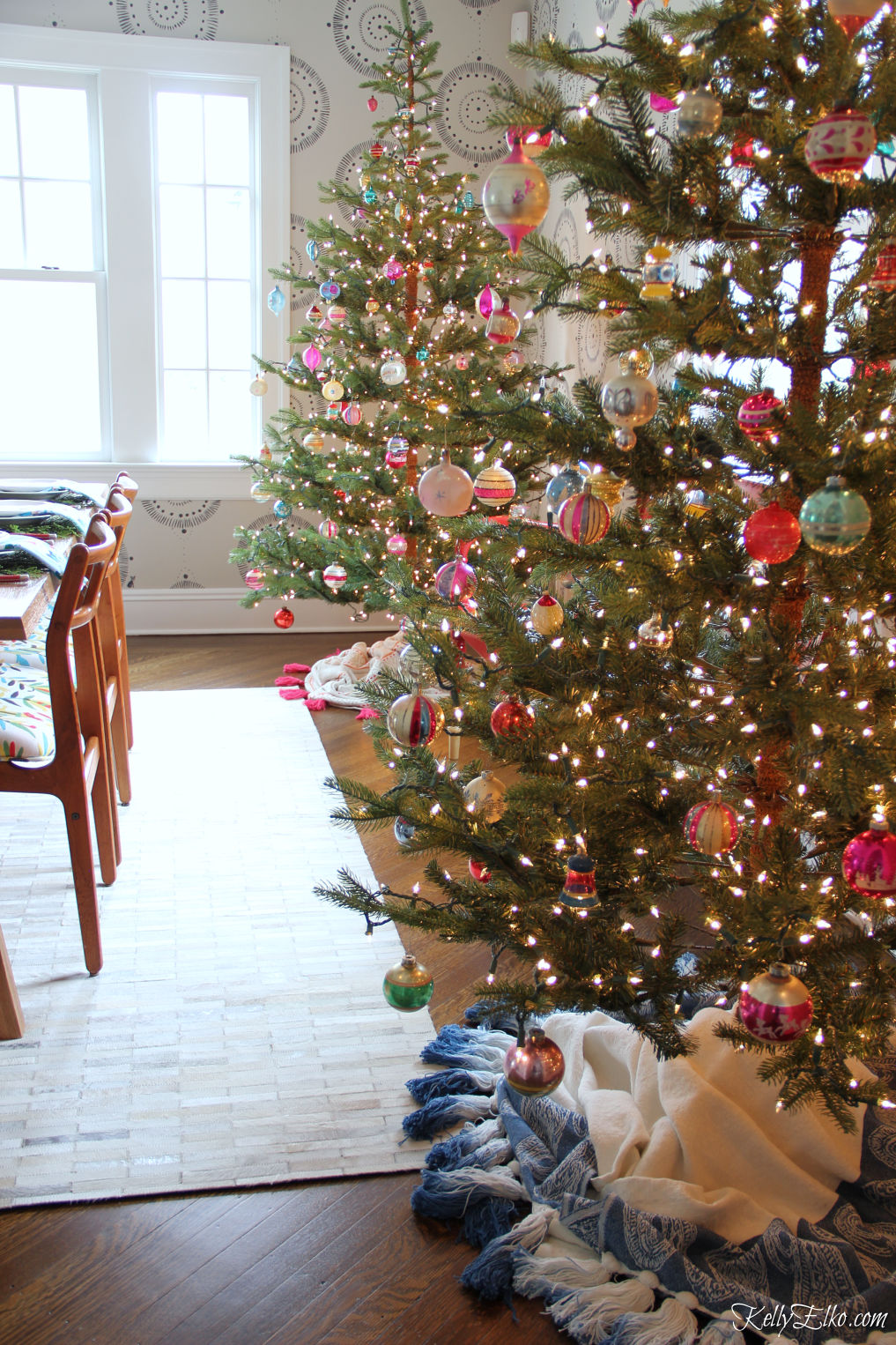 Love this pair of sparse Christmas trees filled with vintage Shiny Brites in this retro Christmas dining room kellyelko.com #christmasdecor #christmasdecorations #christmastrees #vintagechristmas #christmasornaments #shinybrites #retrochristmas #diytreeskirt #treeskirt #christmaslights #gofinding 