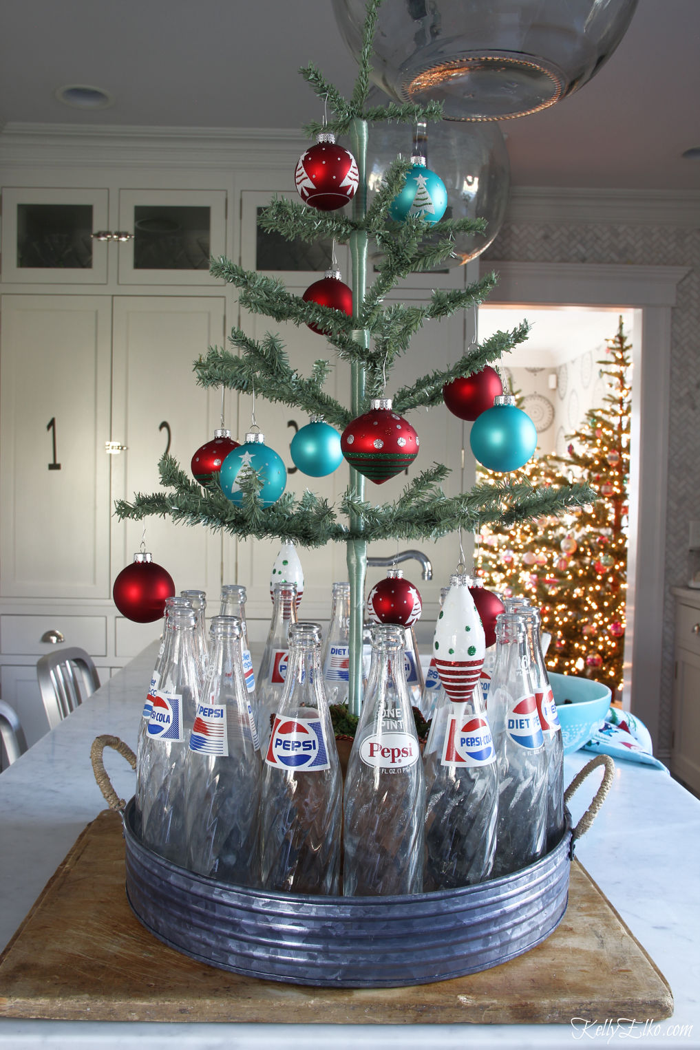 She always has the best Christmas ideas like this feather tree surrounded by vintage Pepsi bottles kellyelko.com #christmas #christmastree #christmasdecor #christmasdecorations #vintagechristmas #christmaskitchen #christmasornaments #farmhousechristmas #diychristmas #christmascrafts