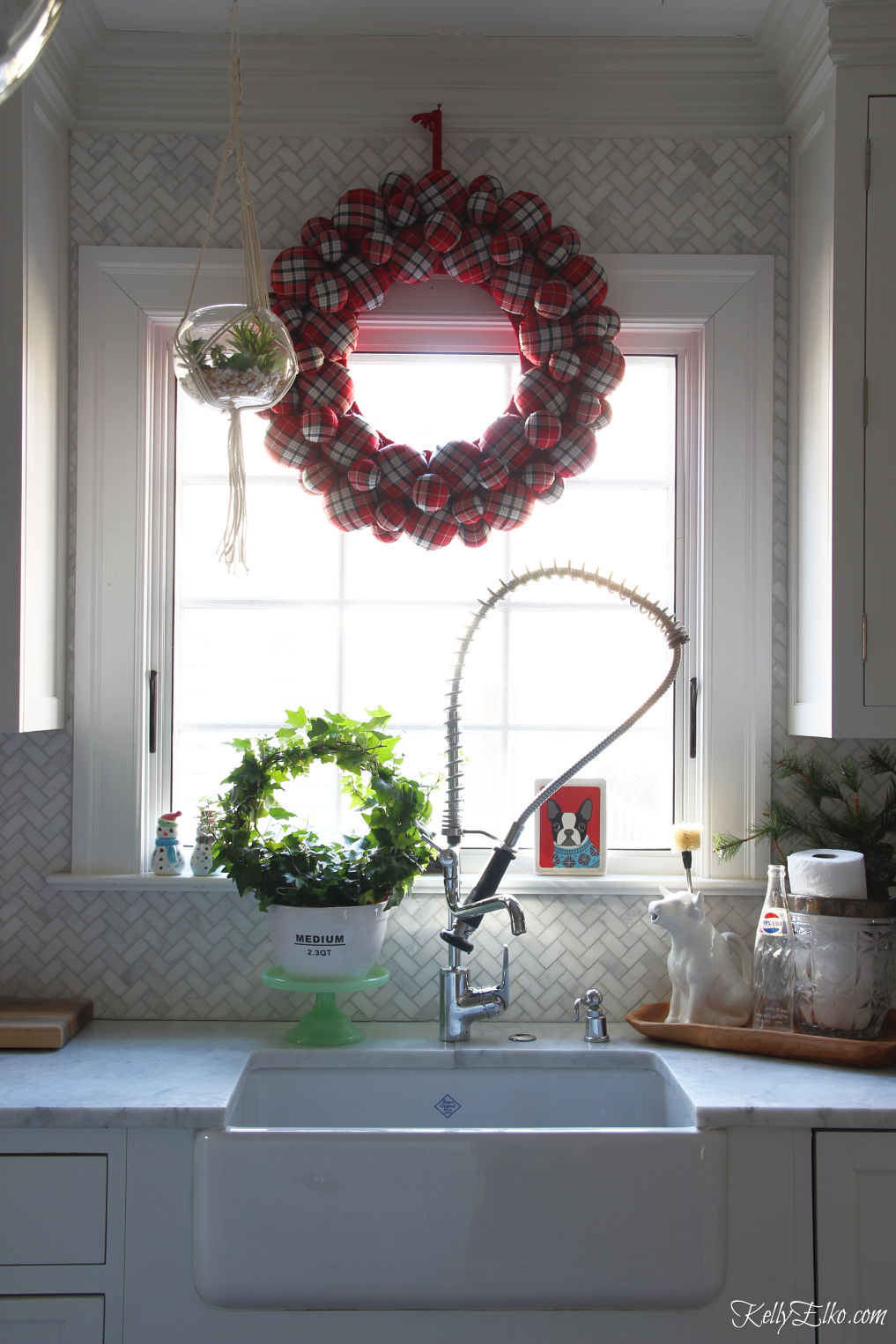 Love this huge plaid wreath in this Christmas kitchen kellyelko.com #christmaskitchen #christmaswreath #plaid #plaidchristmas #farmhousechristmas #whitekitchen #kitchensink 