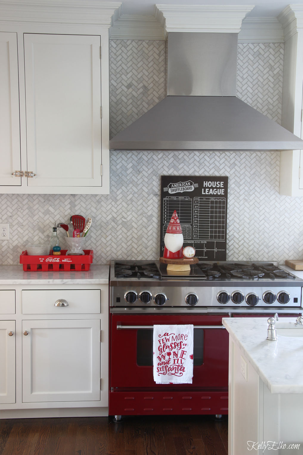 Love this red stove and white herringbone backsplash in this fun Christmas kitchen kellyelko.com #whitekitchen #herringbonetile #backsplash #christmaskitchen #christmasdecor #christmasdecorating #vintagechristmas 