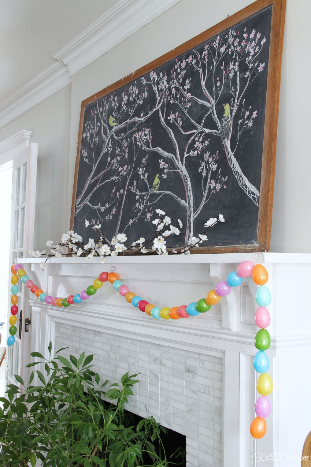 Spring chalkboard mantel - love the original chalk art on the vintage chalkboard and the DIY egg garland kellyelko.com #easter #easterdecor #spring #springdecor #mantel #springmantel #eastereggs #diycrafts #eastercrafts #springcrafts #lighting #plants 