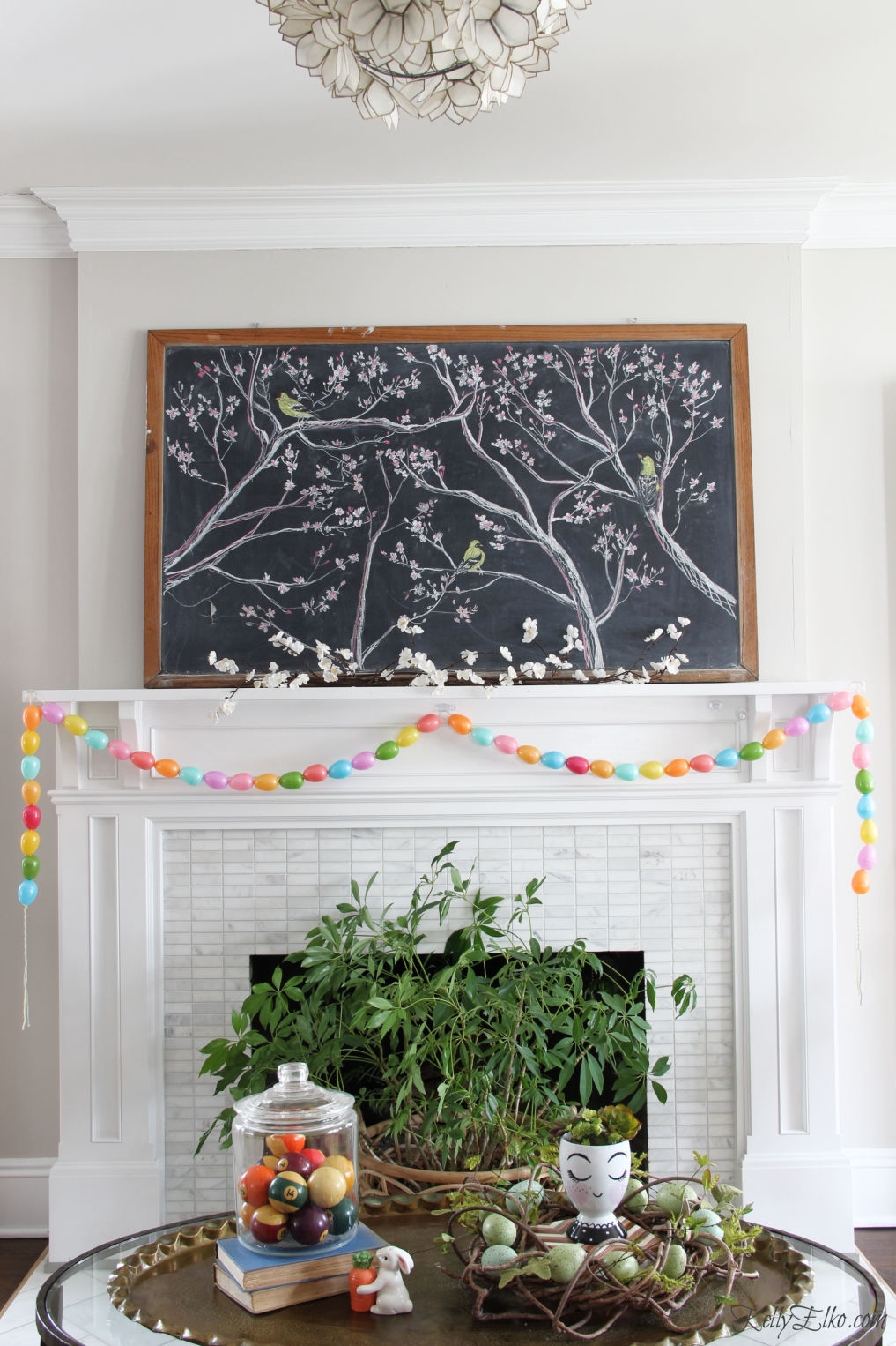 Spring chalkboard mantel - love the original chalk art on the vintage chalkboard and the DIY egg garland kellyelko.com #easter #easterdecor #spring #springdecor #mantel #springmantel #eastereggs #diycrafts #eastercrafts #springcrafts #lighting #plants 