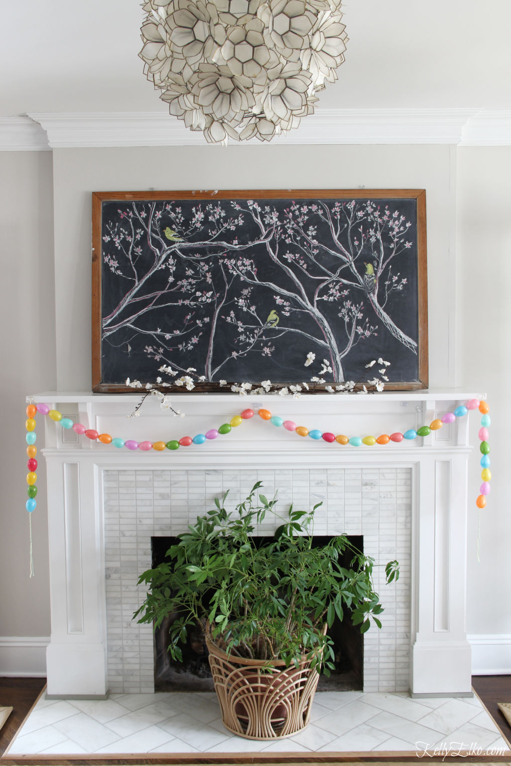 Spring chalkboard mantel - love the original chalk art on the vintage chalkboard and the DIY egg garland kellyelko.com #easter #easterdecor #spring #springdecor #mantel #springmantel #eastereggs #diycrafts #eastercrafts #springcrafts #lighting #plants 