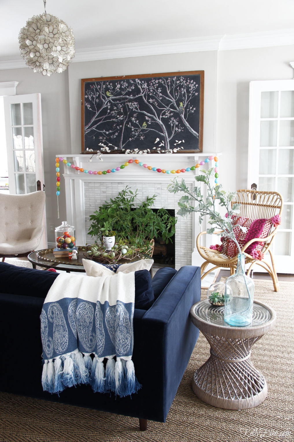 Spring chalkboard mantel - love the original chalk art on the vintage chalkboard and the DIY egg garland kellyelko.com #easter #easterdecor #spring #springdecor #mantel #springmantel #eastereggs #diycrafts #eastercrafts #springcrafts #lighting #plants #rattan #boho #bohodecor 