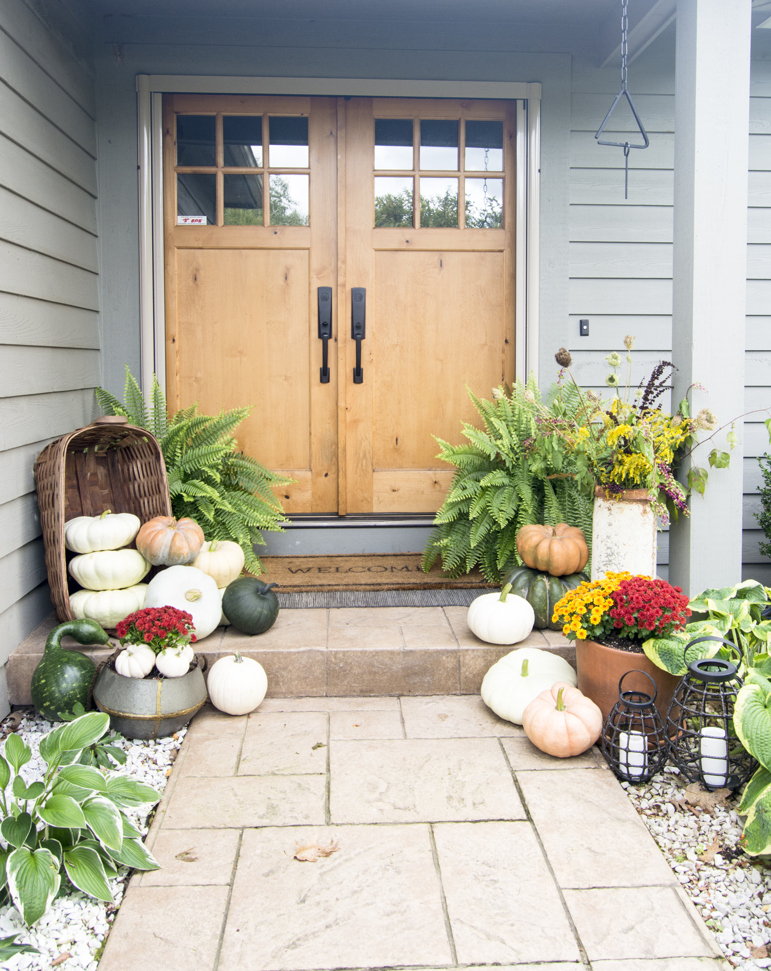 Love the wood double front doors and the pile of pumpkins spilling out of baskets on this fall front porch kellyelko.com #frontporch #porchdecor #pumpkins #falldecor #fallporch 