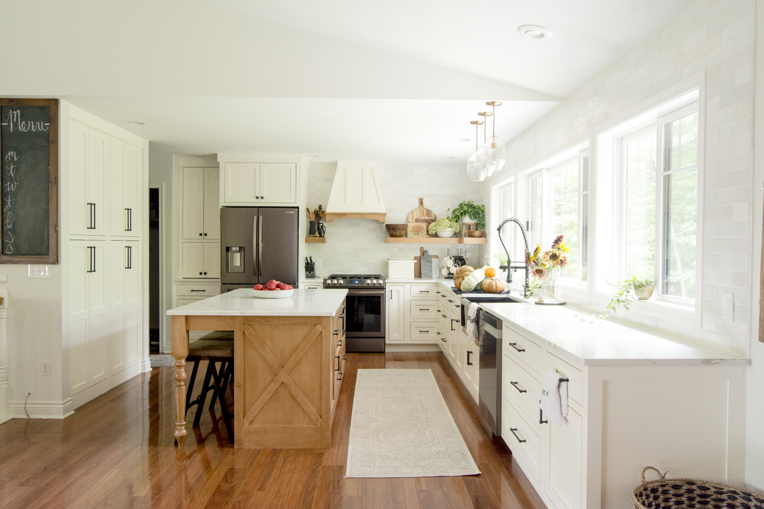 Beautifully renovated kitchen with white cabinets, huge windows and natural wood island kellyelko.com #kitchen #farmhousekitchen #kitchenreno #kitchendecor #kitchendesign #kitchenisland 