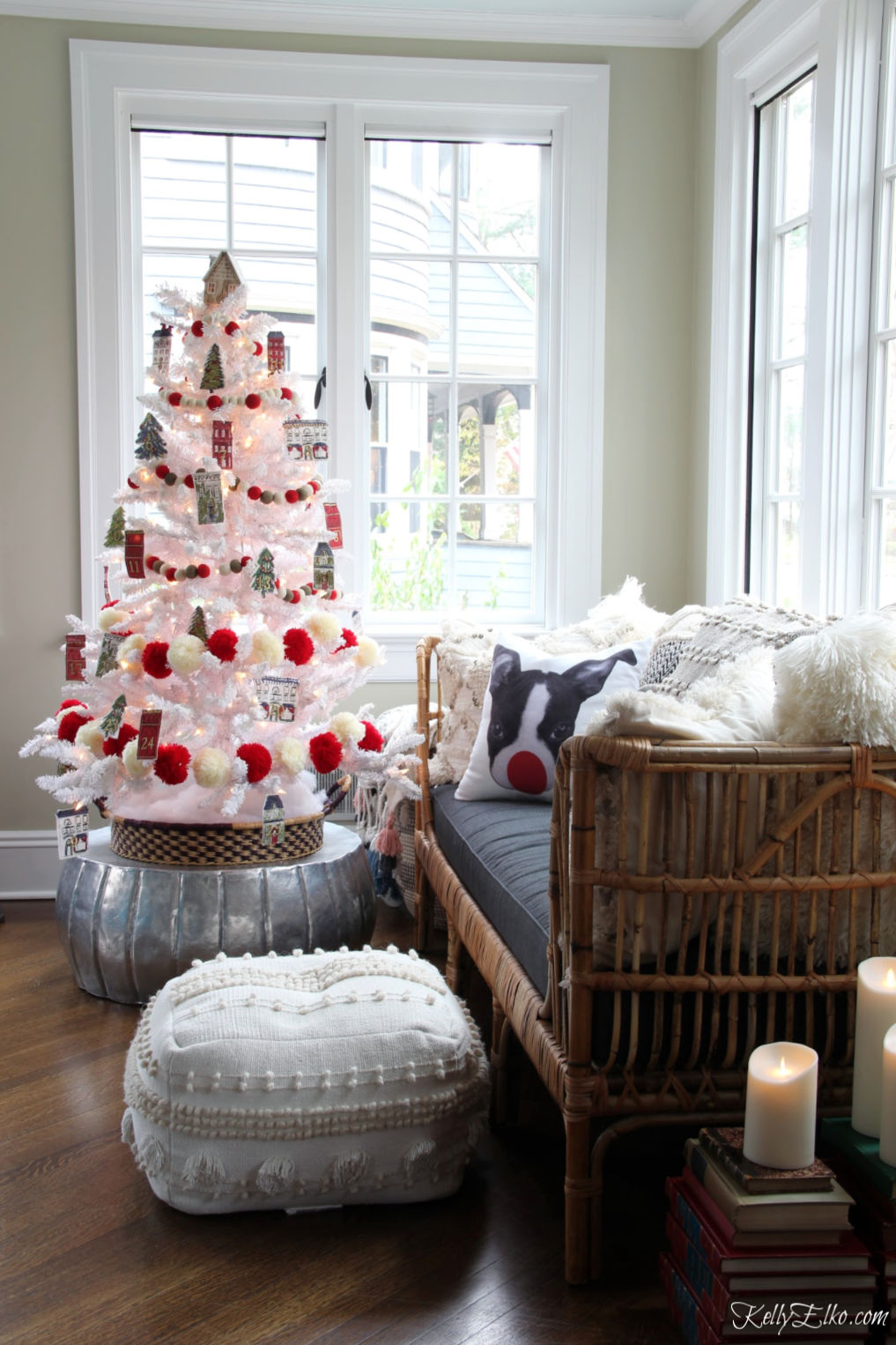 Love this sunroom decked out with a flocked white Christmas tree covered in red and white pom pom garland and Advent countdown ornaments kellyelko.com #sunroom #christmassunroom #rattan #daybed #pouf #christmasdecor #christmastree #christmasornaments #christmasdecorations #diychristmasideas #flockedtree #cozychristmas