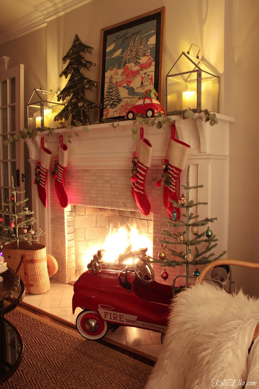 Beautiful Christmas Night Tour and love the roaring fire and festive red pedal car kellyelko.com #christmasdecor #christmasnightstour #christmasmantel #christmaslights #fireplace #roaringfire #vintagechristmas #farmhousechristmas #colorfulchristmas #kellyelko #christmasart #christmassgtockings #feathertrees