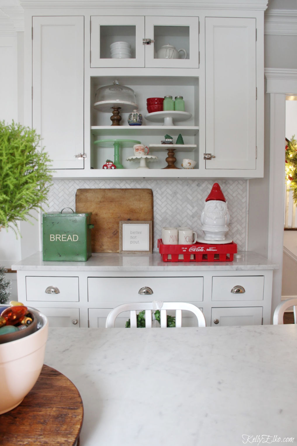 Christmas Home Tour - love the open shelves in this white kitchen decorated in red and green kellyelko.com #christmas #christmasdecor #christmasdecorating #christmashome #christmastour #diychristmas #christmasideas #christmasmantel #christmastree #christmasornaments #vintagechristmas #farmhousechristmas #colorfulchristmas #creativechristmas #kellyelko #christmaskitchen #vintagedecor #breadbox #gnome #openshelves