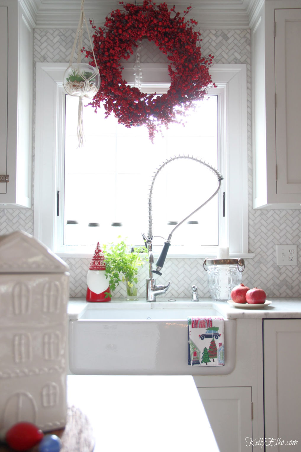 Christmas Home Tour - love the red berry wreath over the kitchen window and the gnome cookie jar in this beautiful white kitchen kellyelko.com #christmas #christmasdecor #christmasdecorating #christmashome #christmastour #diychristmas #christmasideas #christmasmantel #christmastree #christmasornaments #vintagechristmas #farmhousechristmas #colorfulchristmas #creativechristmas #kellyelko #whitekitchen #marbletile #kitchenwindow #berrywreath #christmaswreath #christmaskitchen