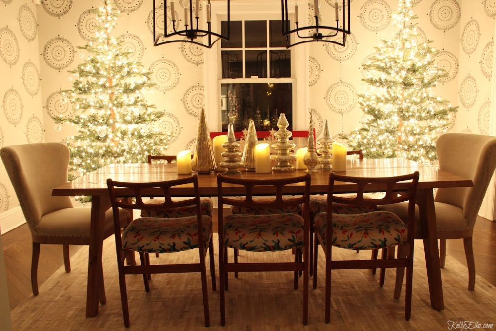 Christmas Nights Tour - love the two glowing trees in the dining room and the mercury glass centerpiece kellyelko.com #christmasdecor #christmastrees #christmasdiningroom #sparsechristmastree #christmaslights #cozychristmas #christmastable #christmascenterpiece #farmhousechristmas #fixerupperstyle #kellyelko #mercuryglass #danishmodern #eclecticstyle #wallmural 