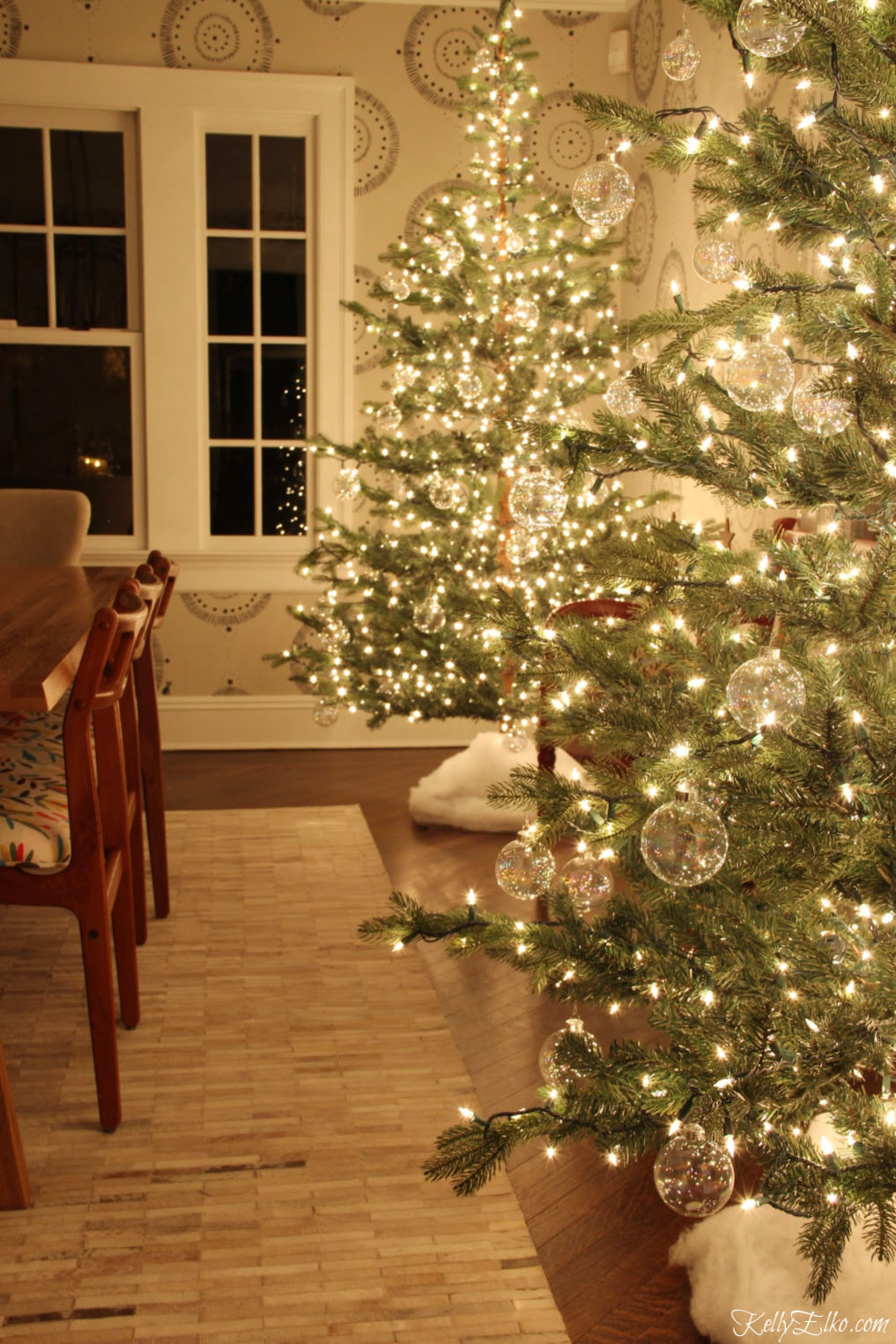 Glowing Christmas Tour at Night - love the pair of glowing sparse trees with clear glass ornaments kellyelko.com #christmasdecor #christmastrees #sparsechristmastrees #christmaslights #christmasdiningroom #christmasornaments #clearornaments #diychristmas #christmascrafts #kellyelko #farmhousechristmas #fixerupperstyle 