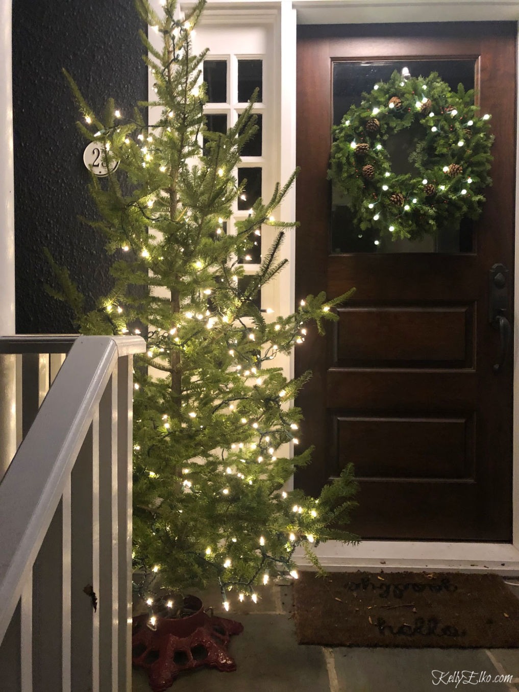 Love this real Christmas tree on the front porch kellyelko.com #christmastree #livechristmastree #christmasporch #christmasporchdecor #christmaslights #sparsetree #kellyelko