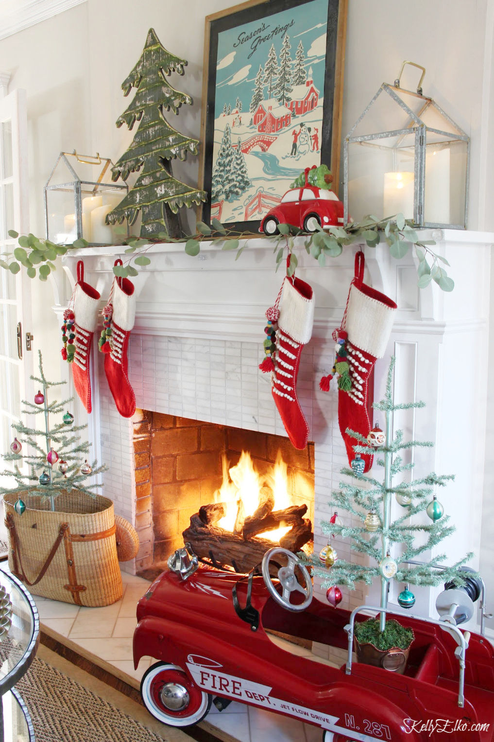 Festive Christmas Decorating Ideas - love this whimsical mantel with vintage firetruck pedal car and red stockings kellyelko.com #christmas #christmasdecor #christmasmantel #christmasstockings #vintagechristmas #feathertrees #fireplace #kellyelko