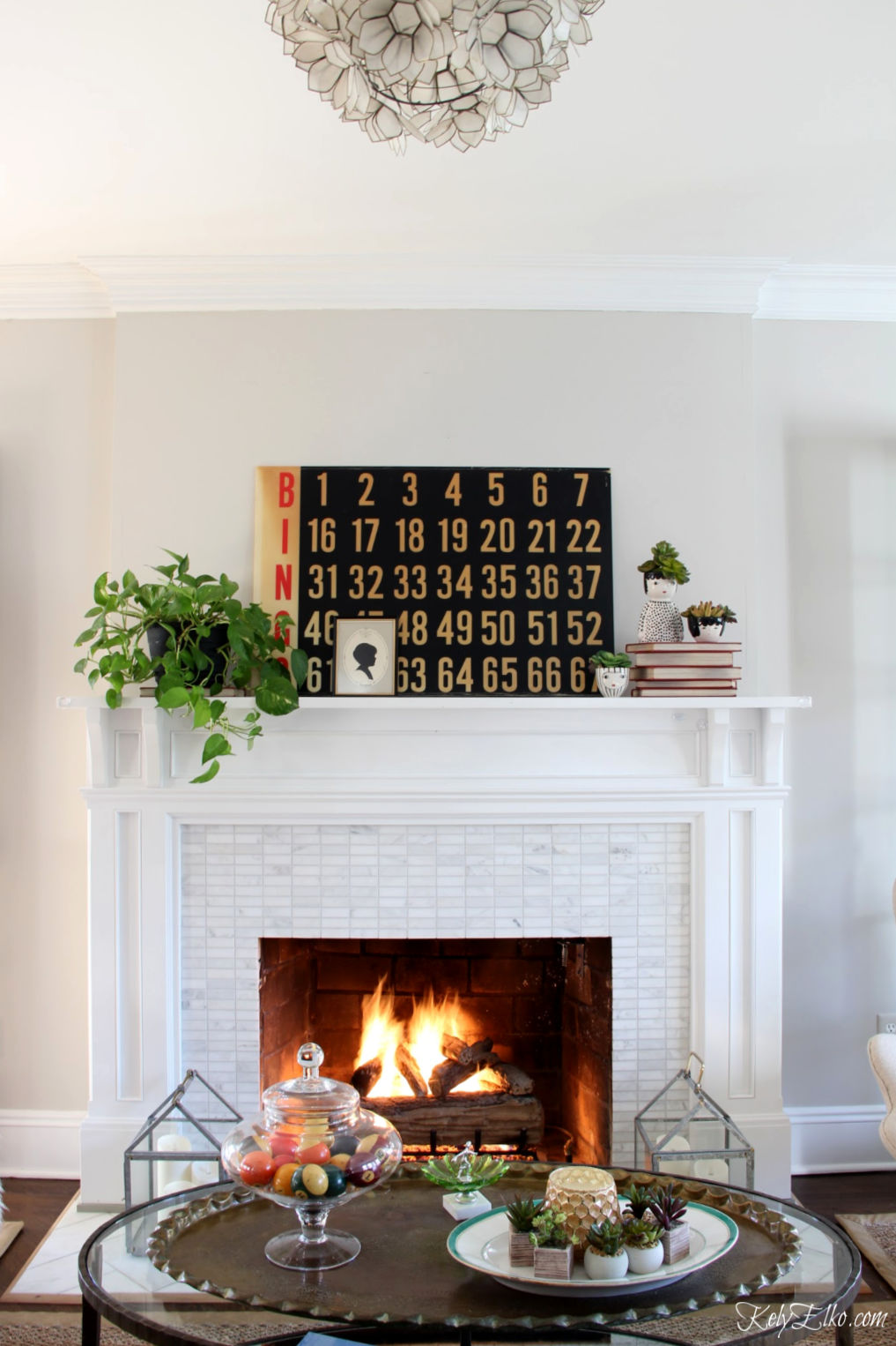 Vintage modern mantel decor - love the huge old bingo board and black white red and green color palette kellyelko.com #mantel #manteldecor #vintagedecor #vintagemantel #wintermantel #vintagedecorating #thriftedecor #thriftydecor #plantlady #houseplants #succulents #farmhousemantel #farmhousedecor #eclecticdecor #fireplacedecor #kellyelko