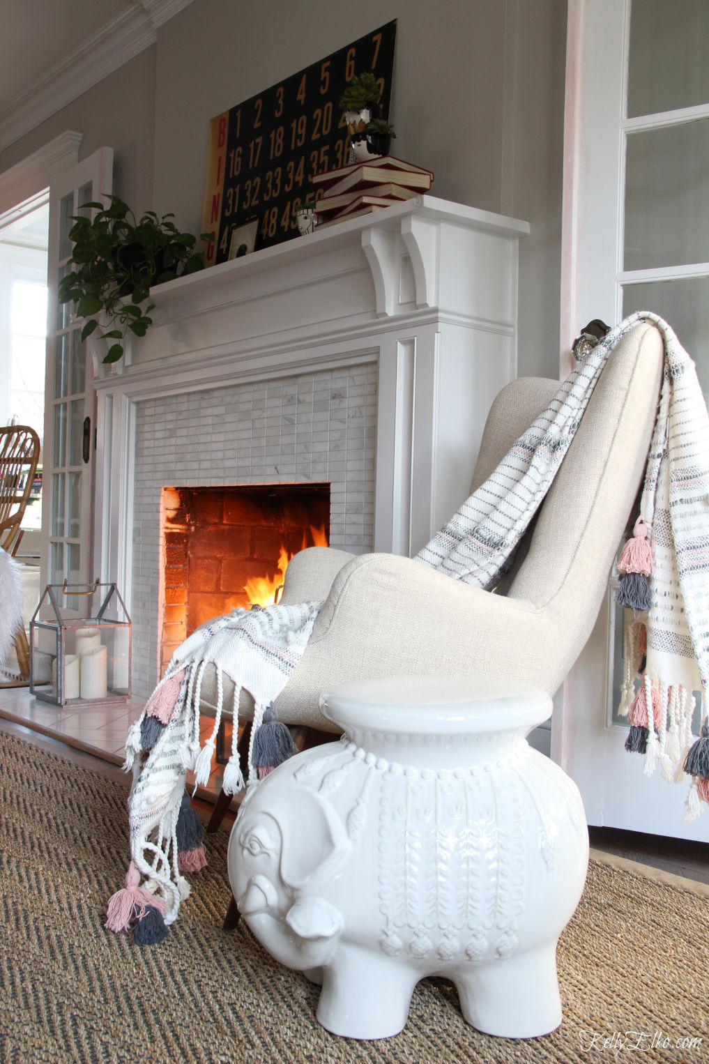 Love this mantel in black and white with a vintage bingo scorecard and the adorable elephant stool and tassel throw kellyelko.com #livingroomdecor #bohodecor #eclecticdecor #elephant #vintagemodern #mantel #manteldecor #fixerupperstyle #farmhousedecor #kellyelko.com #fireplacedecor #cozydecor