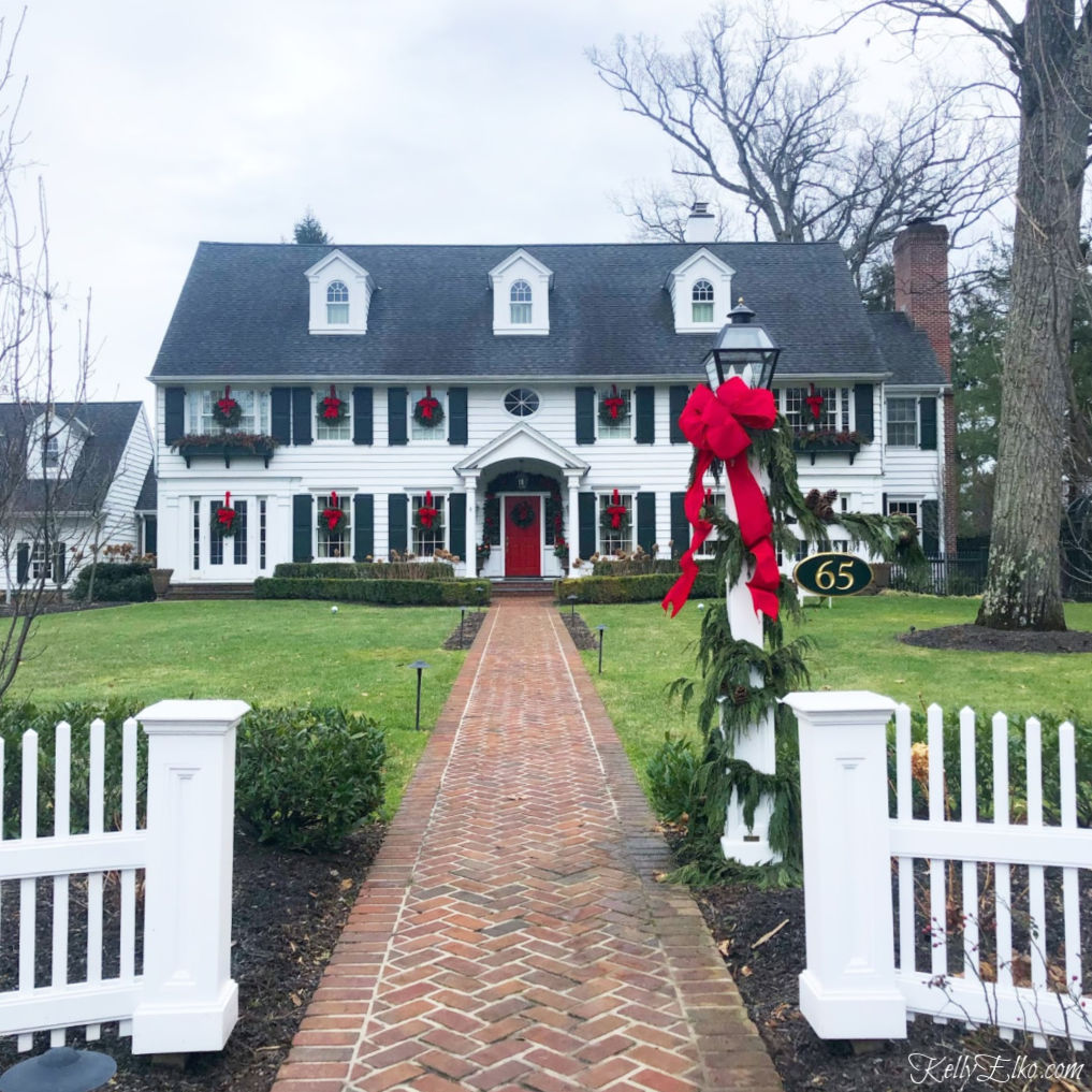 Classic white house with black shutters decked out for Christmas. Love the outdoor wreaths with festive red bows kellyelko.com #christmas #christmasdecor #outdoorchristmasdecor #christmashouse #christmaswreath #classicchristmas #christamsdecoratingideas #outdoorchristmasdecorations #kellyelko #oldhouse 