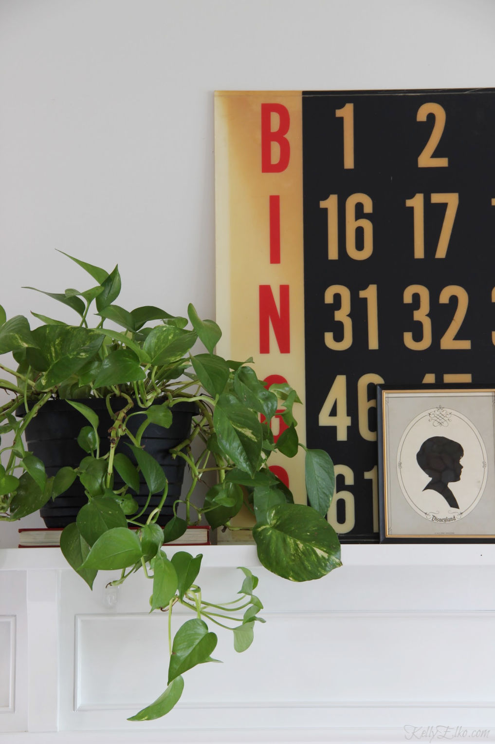 Love this vintage inspired mantel in black and white with touches of green from a pothos plant kellyelko.com #mantel #manteldecor #pothos #houseplants #plantlady #vintagedecor #vintagemantel #silhouette #bingo #thriftydecor #thrifteddecor #vintagemodern #farmhousedecor #kellyelko