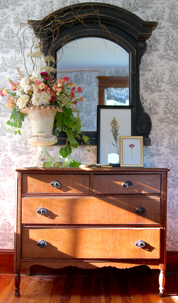 Toile wallpaper is a beautiful backdrop to an antique chest and mirror kellyelko.com #toile #antiques #farmhouse #farmnousedecor #antiquedresser #urn #floralarrangement #countryliving