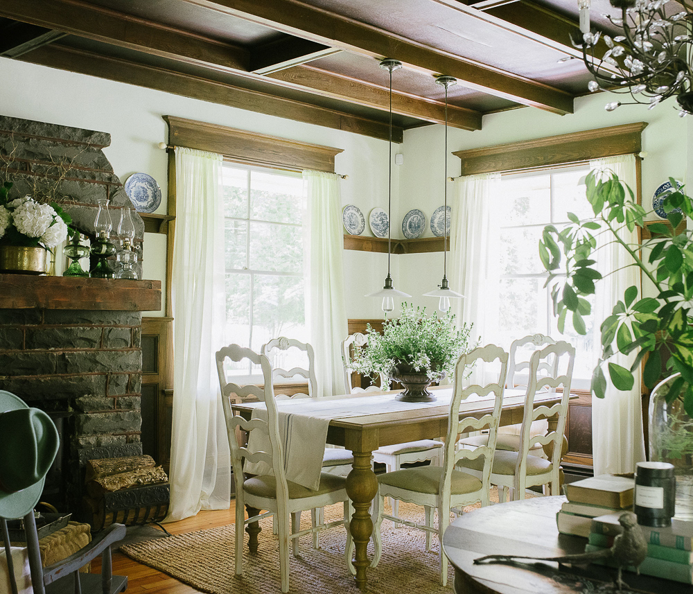 Coffered ceilings in dark wood contrast with white dining chairs and an original old stone fireplace in this charming farmhouse dining room kellyelko.com #diningroom #diningroomdecor #farmhouse #farmhouserdecor #antiques #fireplace #mantel 