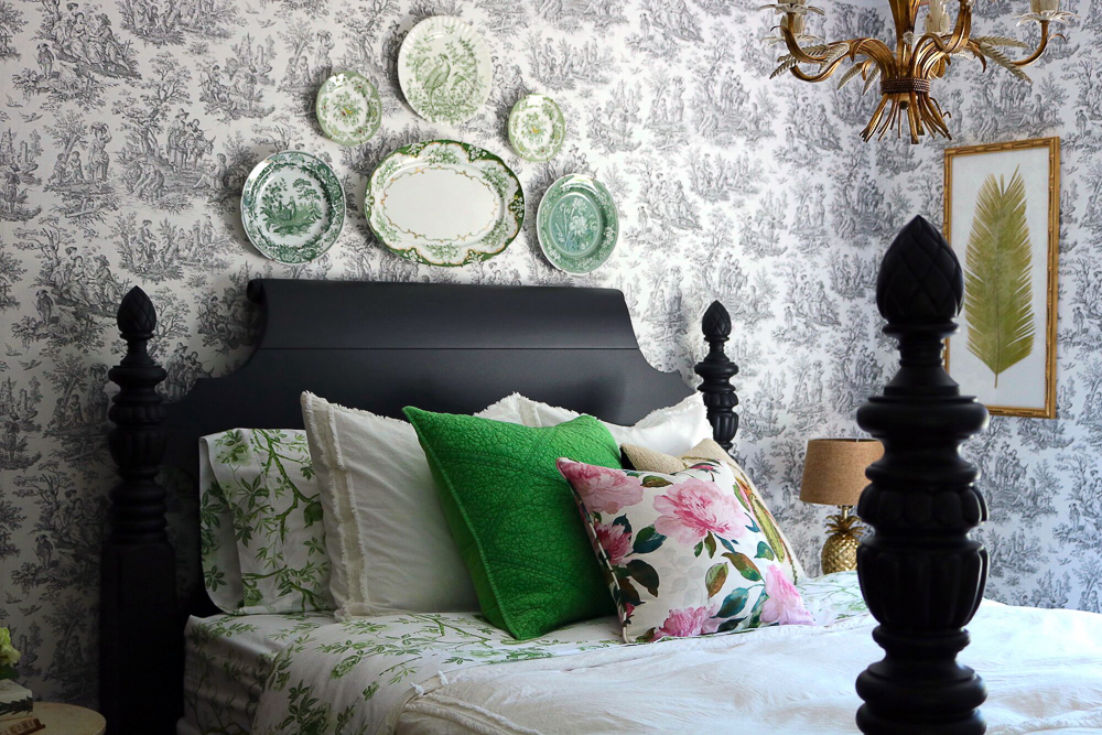 Toile wallpaper is the perfect backdrop to a green plate wall in this guest bedroom kellyelko.com #bedroom #antiquebedroom #farmhouse #farmhousedecor #farmhousebedroom #platewall #antiquebed #antiquefurniture #toile #toilewallpaper 