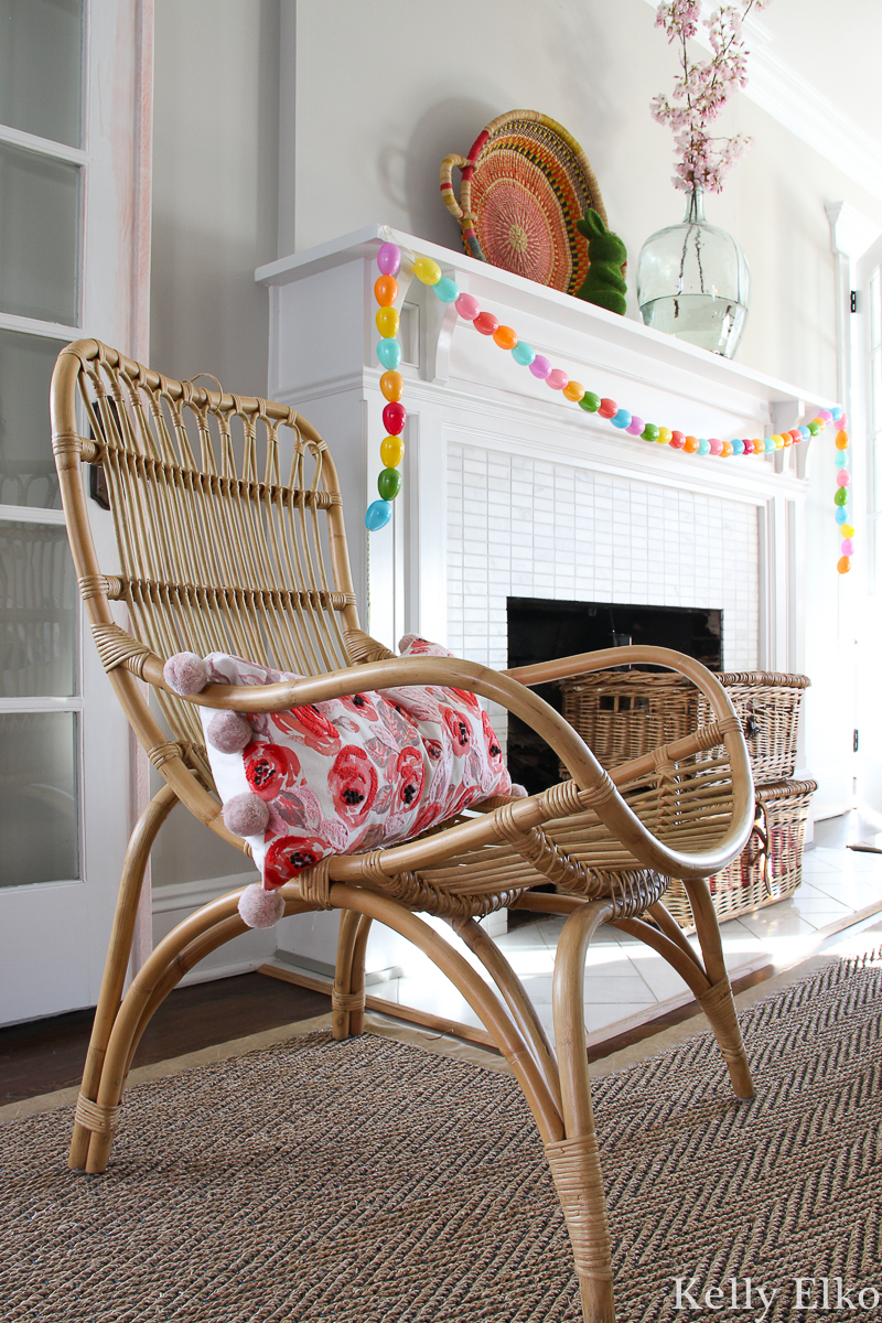 Colorful spring mantel with DIY egg garland and pink peony pillow on a rattan chair kellyelko.com #rattan #peony #spring #springdecor #springmantel #diycrafts #eastercrafts #springcrafts #eclecticdecor #kellyelko