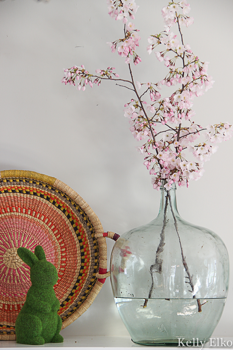 Beautiful spring mantel with flowering cherry blossom branches in a vintage glass jug kellyelko.com #spring #springdecor #cherryblossom #floweringtrees #floweringbranch #bohodecor #easterbunny #vintagedecor #farmhousedecor 