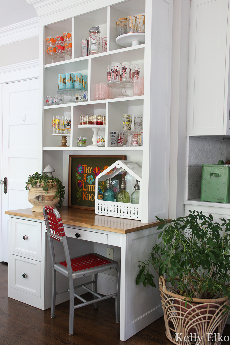 Love this colorful vintage drinking glass display in this white kitchen with farmhouse plate rack and bubble chandelier kellyelko.com #vintageglass #vintageglasses #drinkingglasses #vintagedrinkingglass #collectibles #collections #collect #collector #kitchendecor #vintagedecor #colorfuldecor #thrifted #vintagemodern #shelfie #kellyelko #kitchen #platerack #mugrack #farmhousedecor #farmhousekitchen