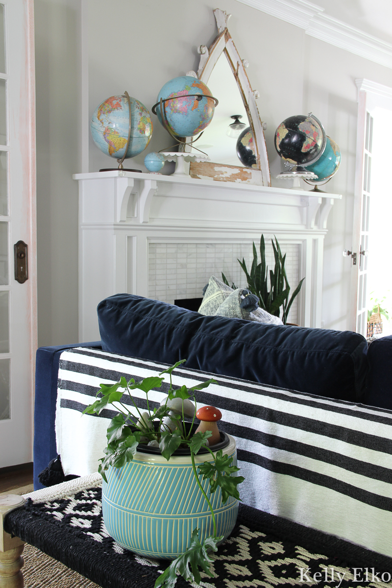 Eclectic living room with vintage globe collection and lots of boho texture from tassel throws and woven benches and plants kellyelko.com #vintagedecor #eclecticdecor #bohodecor #plantlady #houseplants #collections #vintagecollection #globes #manteldecor #farmhousedecor #interiordecor #manteldecor 