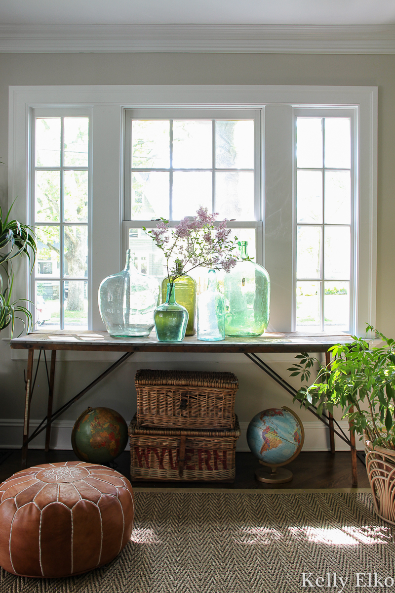 Beautiful antique wallpaper pasting table with a collection of vintage glass demijohns kellyelko.com #antiques #antiquedecor #vintagedecor #eclecticdecor #demijohn #collections #collect #vintagemodern #bohodecor #plants #houseplants #interiorstyling #kellyelko