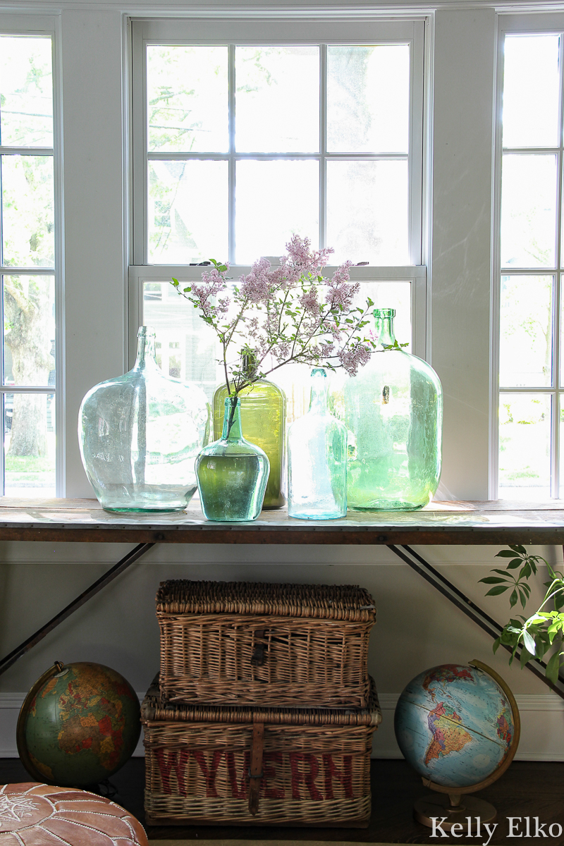 Beautiful antique wallpaper pasting table with a collection of vintage glass demijohns kellyelko.com #antiques #antiquedecor #vintagedecor #eclecticdecor #demijohn #collections #collect #vintagemodern #bohodecor #plants #houseplants #interiorstyling #kellyelko #wicker