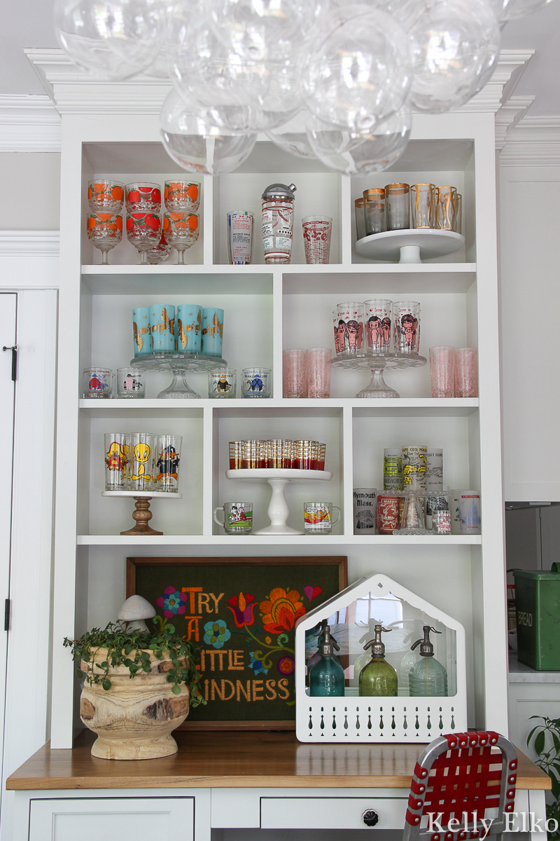 Love this colorful vintage drinking glass display in this white kitchen kellyelko.com #vintageglass #vintageglasses #drinkingglasses #vintagedrinkingglass #collectibles #collections #collect #collector #kitchendecor #vintagedecor #colorfuldecor #thrifted #vintagemodern #shelfie #kellyelko #kitchen 