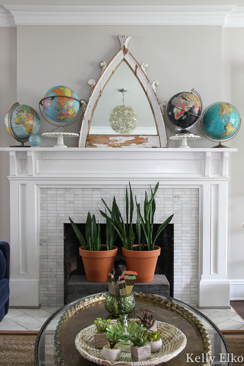 Love this living room with vintage globe collection the mantel and that architectural piece turned mirror kellyelko.com #mantel #manteldecor #eclecticdecor #vintagedecor #globes #vintageglobes #bohodecor #plants #houseplants #fireplacedecor #vintagemodern #interiordecor #kellyelko