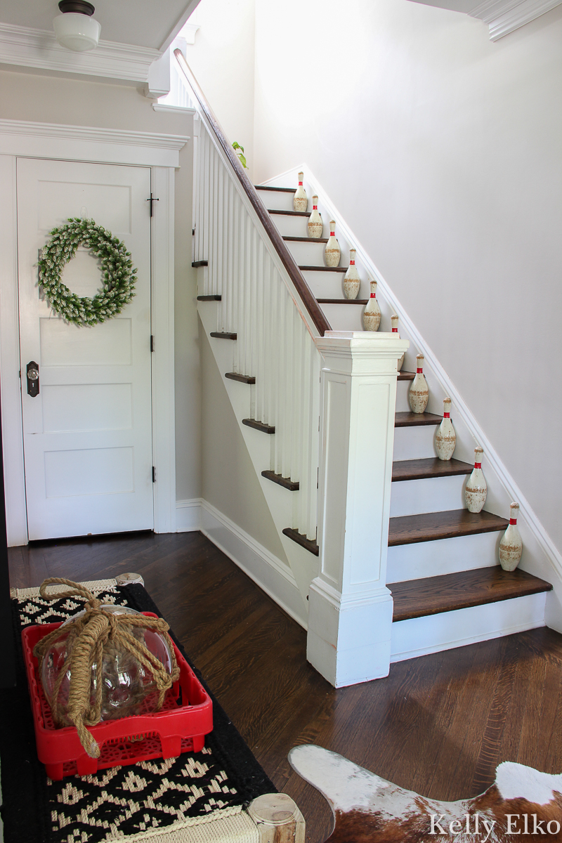 Love the vintage bowling pins on the staircase of this farmhouse foyer kellyelko.com #vintage #vintagedecor #bowlingpins #farmhouse #farmhousedecor #farmhouseentry #foyer #foyerdecor #staircasedecor #graypaint #neutraldecor #summerdecor #eclecticdecor #collections #collector #thrifted 