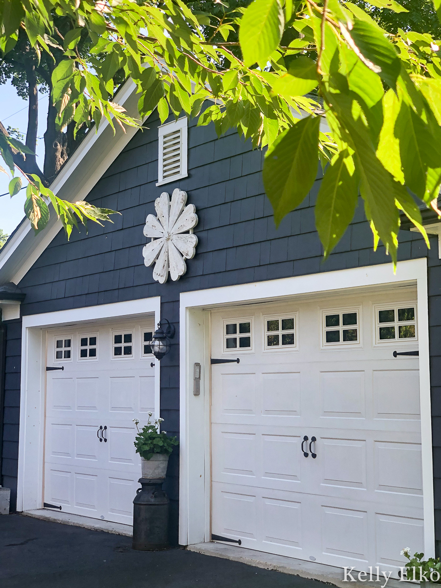 Love this giant barn wood flower hung on the garage for instant curb appeal kellyelko.com #garage #outdoordecor #farmhousedecor #farmhousestyle #whiteflower #curbappeal #halenavy #bluepaint #paintcolors #exteriorpaintcolors #garagedoors 