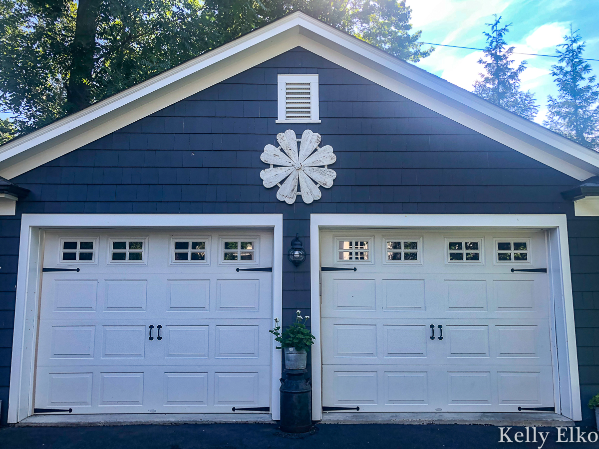 Love this giant barn wood flower hung on the garage for instant curb appeal kellyelko.com #garage #outdoordecor #farmhousedecor #farmhousestyle #whiteflower #curbappeal #halenavy #bluepaint #paintcolors #exteriorpaintcolors #detachedgarage