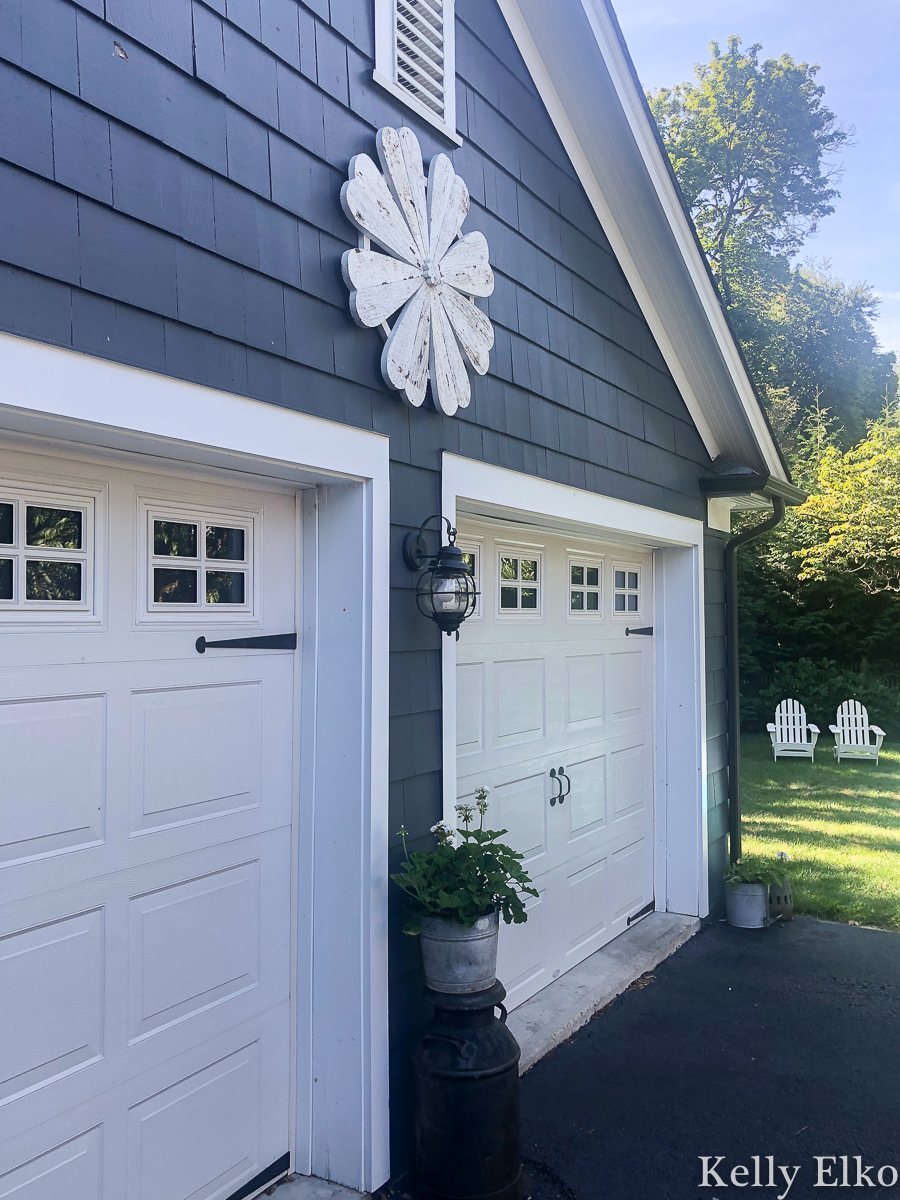 Love this huge barn wood flower that adds so much curb appeal to this garage kellyelko.com #barnwood #farmhouse #farmhousedecor #farmhousestyle #garage #halenavy #bluehouse #bluepaint #curbappeal #whiteflower #outdoordecor 