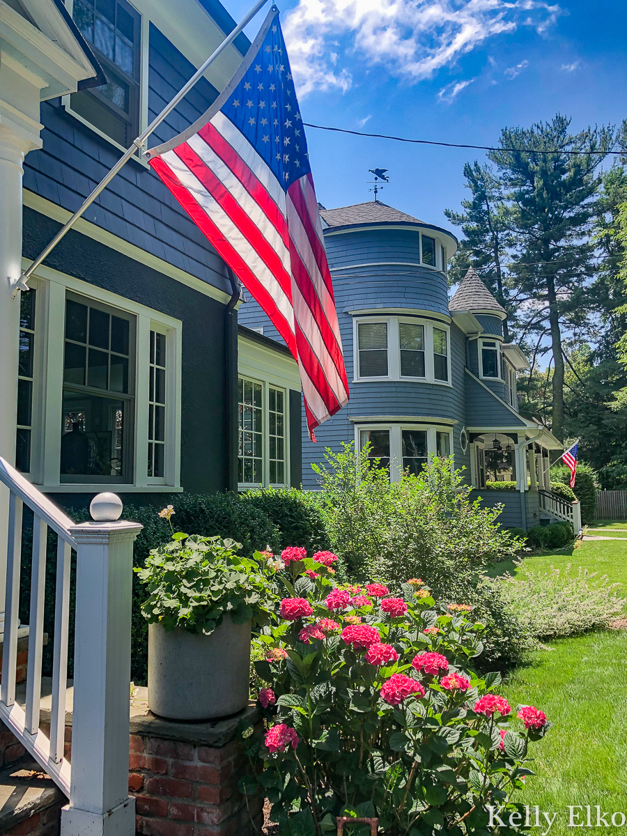 Love an American flag hung on a house kellyelko.com #blue #bluepaint #bluehouse #halenavy #housepaint #housecolors #curbappeal #oldhouse #oldhome #oldhouses #fixerupper #frontporch #landscaping #gardening #gardens #dormers #farmhouse #farmhousedecor