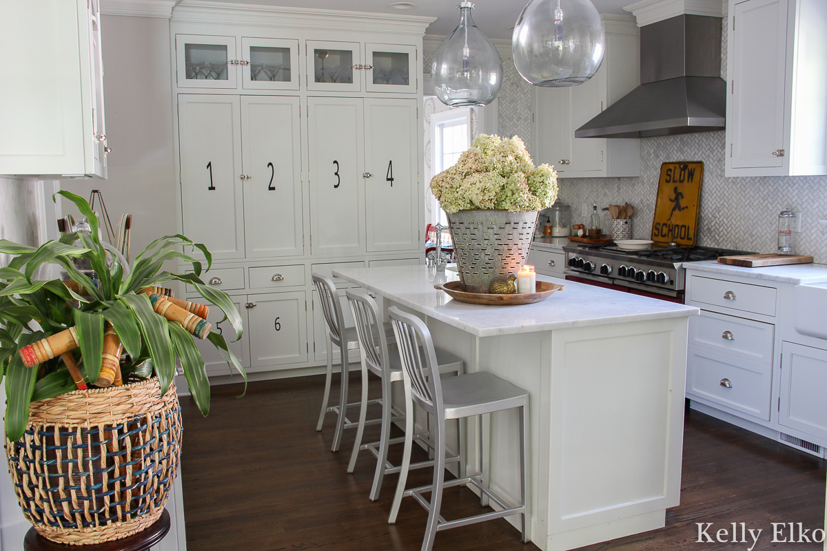 White kitchen with beautiful glass pendant lights and marble counters and backsplash kellyelko.com #whitekitchen #kitchen #farmhousekitchen #whitecabinets #farmhousedecor #kitchendecor #fallkitchen #hydrangeas