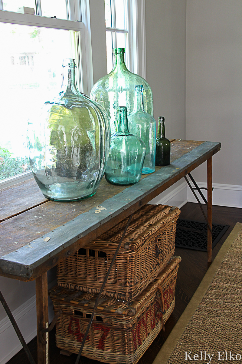 Beautiful collection of vintage demijohn bottles on an old wallpaper pasting table kellyelko.com #vintagedecor #antiquedecor #demijohn #rattan #antiques #falldecor #collections #vintagecollection #vintagedecor 