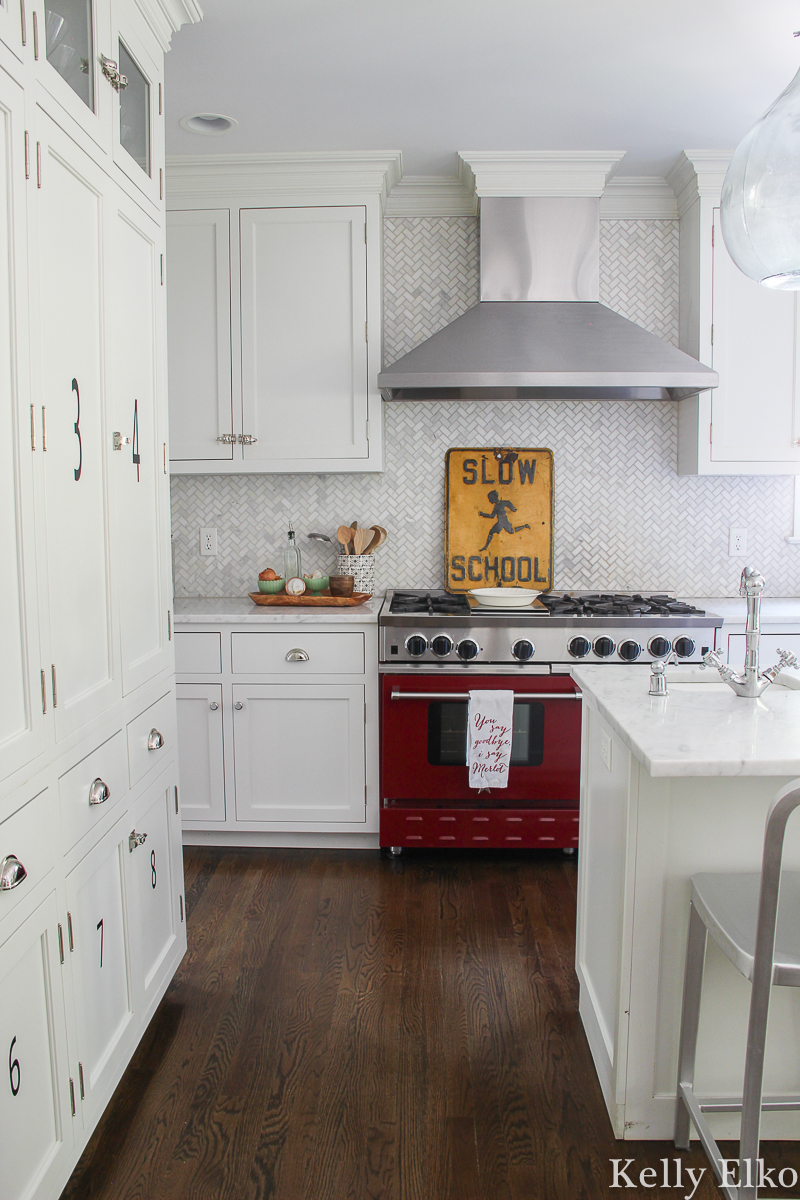 White kitchen with red stove and herringbone marble backsplash kellyelko.com